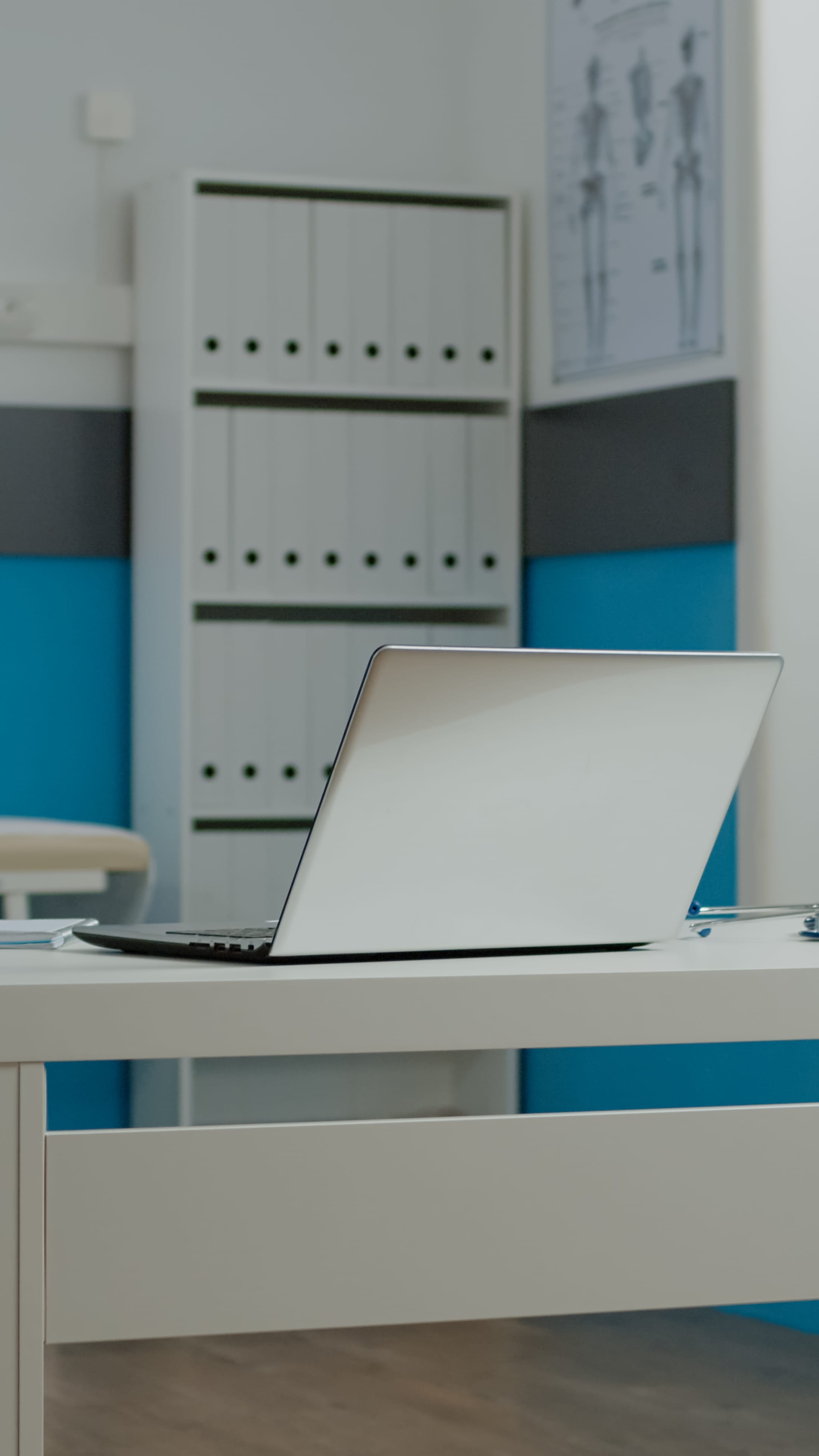 A clinician's laptop on a consulting-room desk, ready for a patient.